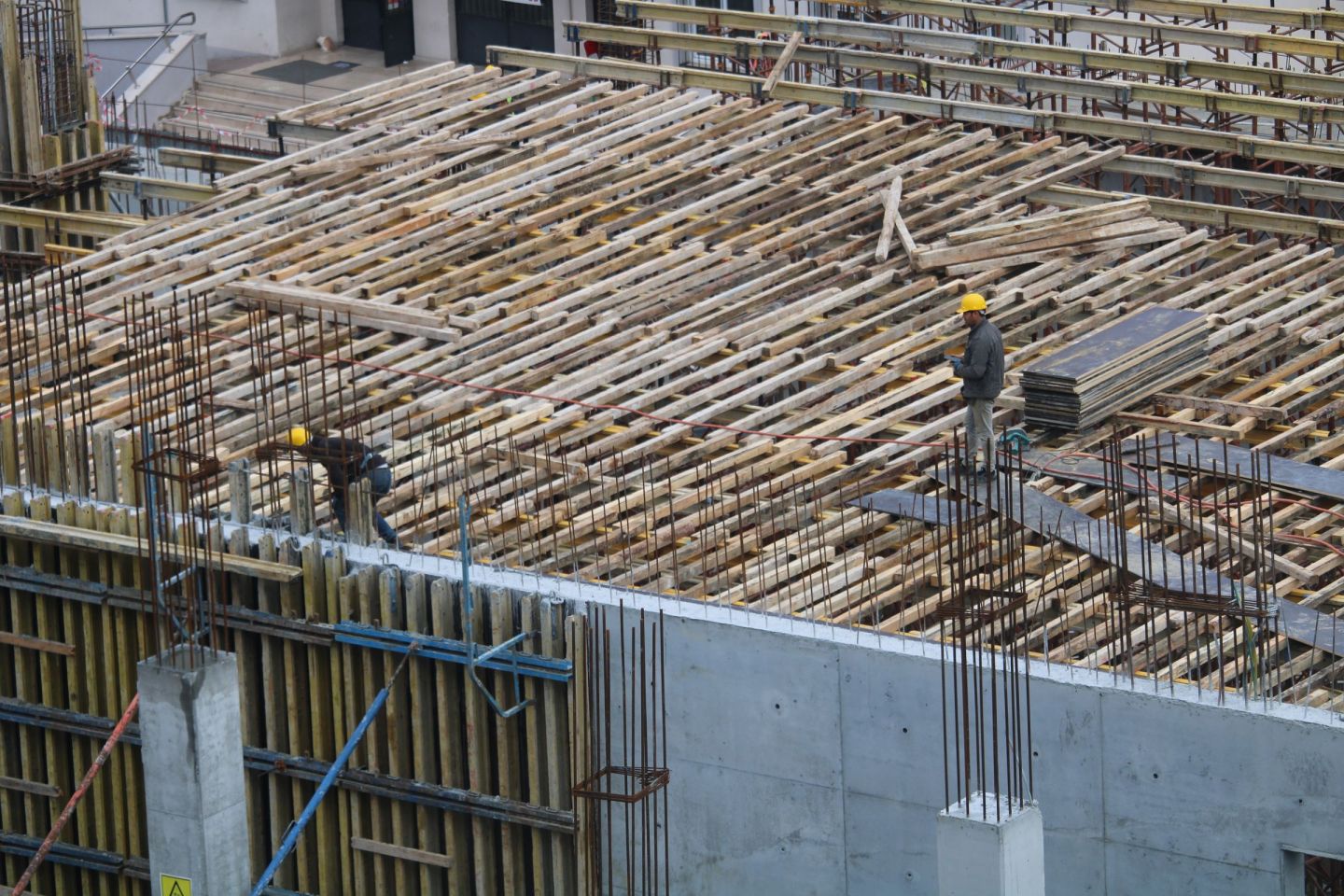 Deckenschalung mit verlegter Bewehrung über einer betonierten Wand, Arbeiter auf der Fläche